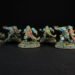 Six teal-armored dwarf miniatures with long braided beards on grassy round bases, labeled with names like Uli Underfoot and Train Thrice-Cursed.