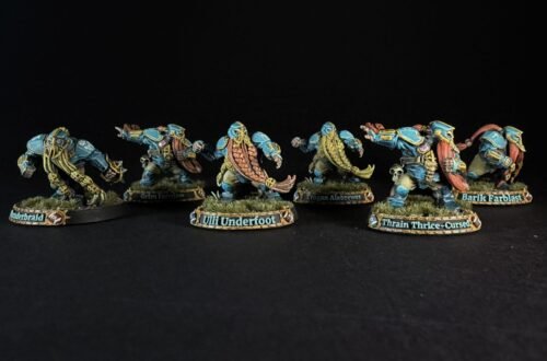 Six painted dwarf miniatures in blue armor stand in a row on grassy bases, with name banners reading Underbraid, Grim Tornjaw, Uli Underfoot, Trogan Alebrew, Train Thrice-Cursed, and Barik Farblast visible on the bases.