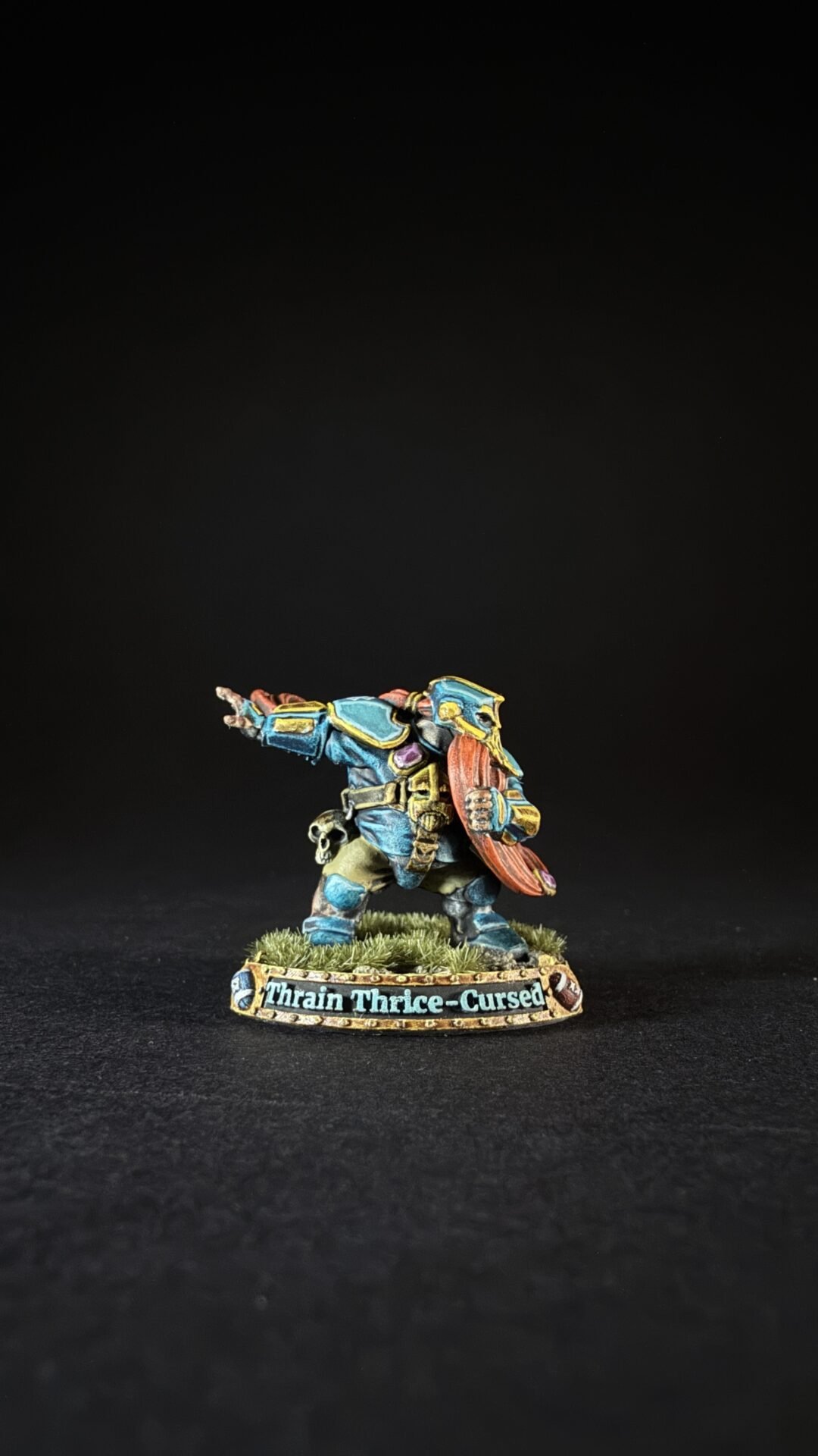Painted miniature of a dwarf warrior in blue armor with a red beard, holding a shield, standing on a grassy base labeled 'Thrain Thrice-Cursed'.