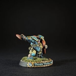 Painted fantasy dwarf miniature in blue armor raising a shield, standing on a grassy base with the name 'Thrain Thrice-C' along the edge