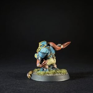 Painted tabletop miniature: blue-armored turtle-like warrior with orange scarf, standing on a grassy sculpted base.
