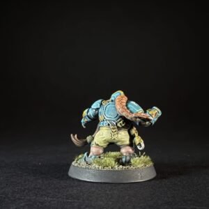 Back view of a fantasy mini with blue armor, yellow trim, and a scorpion-like tail, standing on a grassy textured base.