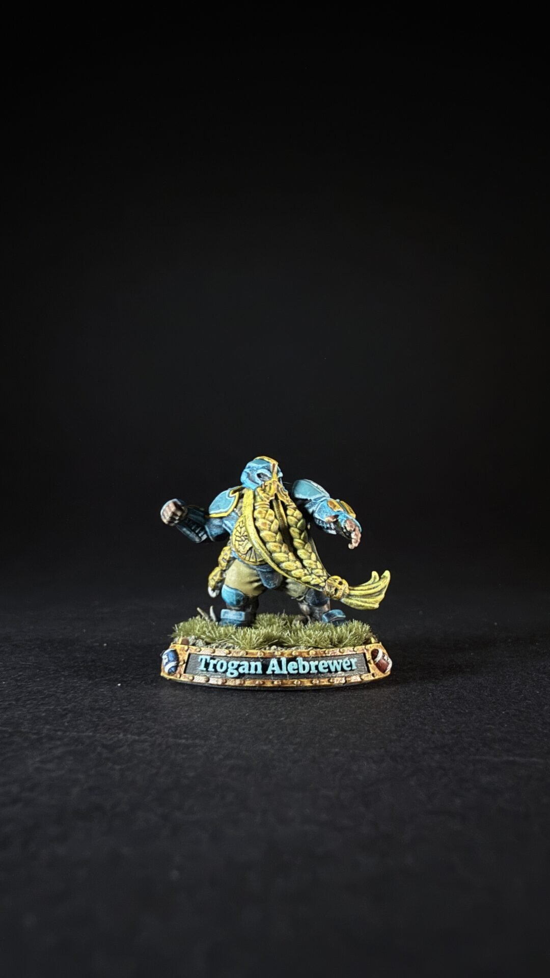 Miniature figure of Trogan Alebrewer, a blue-skinned warrior with gold trim, standing on grassy base.