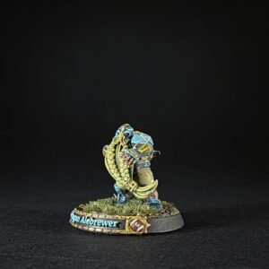 Painted fantasy miniature of a blue-armored dwarf clutching a yellow horned weapon on a grassy round base.