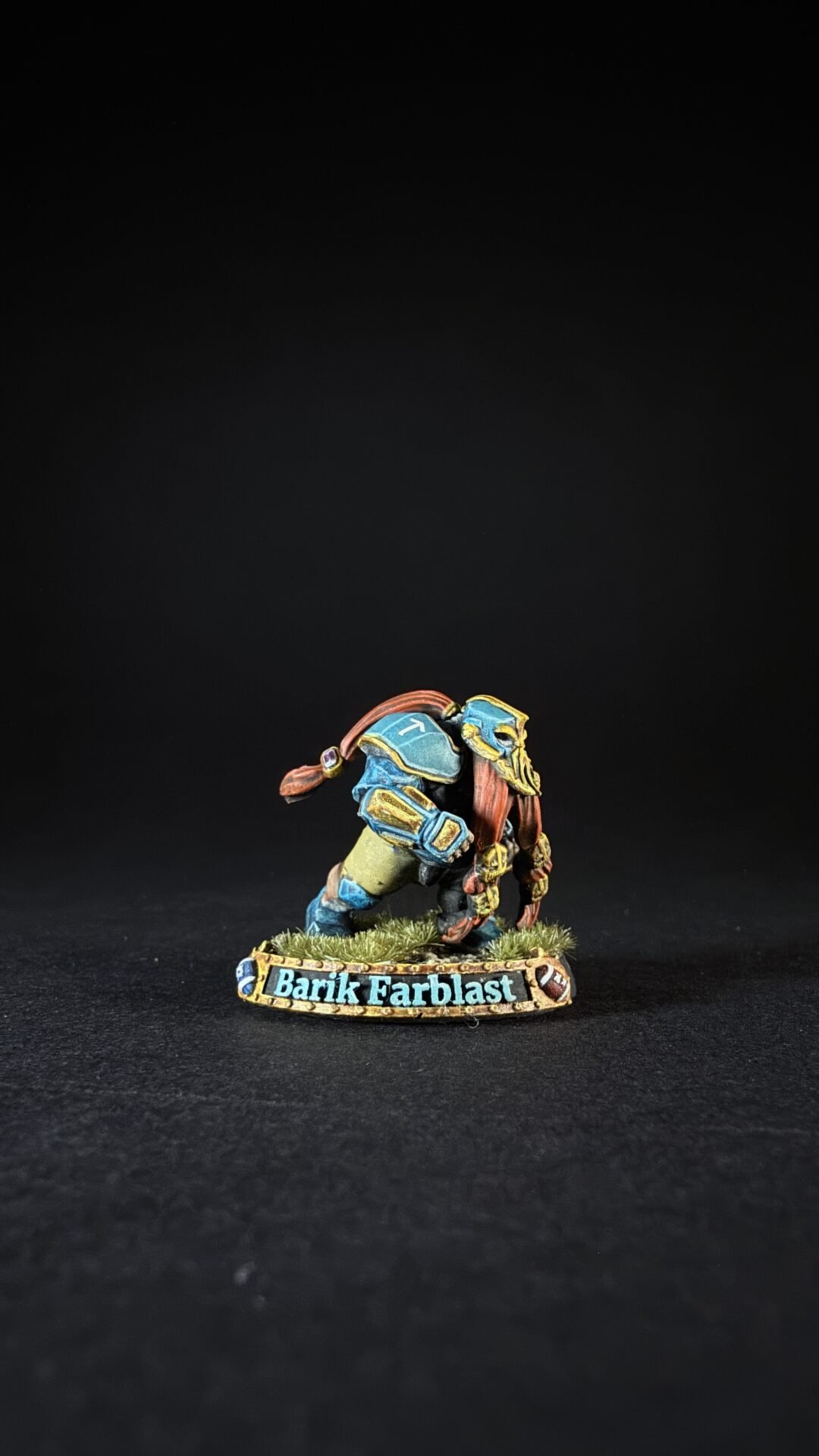 Miniature figure of a muscular armored warrior in blue and gold, crouching on a grassy base marked 'Barik Farblast'.