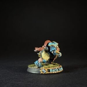 Small painted miniature of Barik Farstrider (or Barik) kneeling on a grassy base with blue and gold armor and red hair, from a tabletop game.