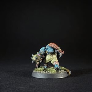 Back view of a painted fantasy dwarf miniature in blue armor with a spiked gauntlet, on a grassy base.