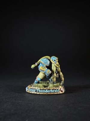 Miniature figure in blue and gold armor kneeling on grass, base labeled 'Grum Thunderbraid'.