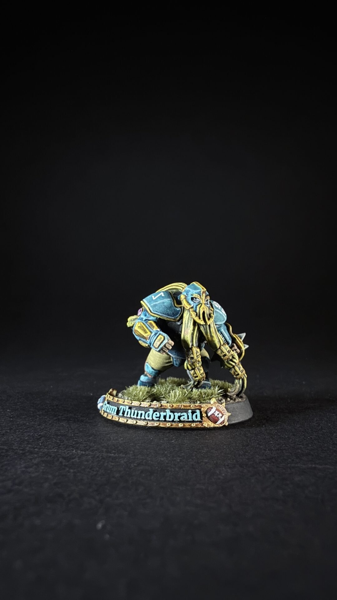 Painted tabletop dwarf miniature in blue and gold armor, wielding twin blades, on a grassy base marked 'Thunderbraid'.