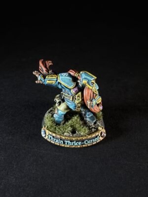 Painted dwarf warrior miniature in blue armor with an orange cape, raising a shield on a grassy rocky base labeled Thrain Thrice-Cursed.