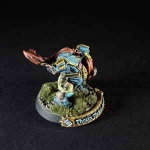Painted fantasy miniature of a teal-blue armored warrior with red cape, standing on a grassy diorama base.