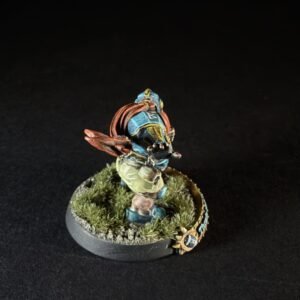 Hand-painted miniature figure of a warrior in blue armor and tan shorts, standing on a grassy gaming base with a small banner/crest nearby.