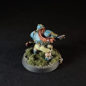 Miniature dwarf warrior in blue armor with a red scarf, standing on a grassy, rocky base (back view).