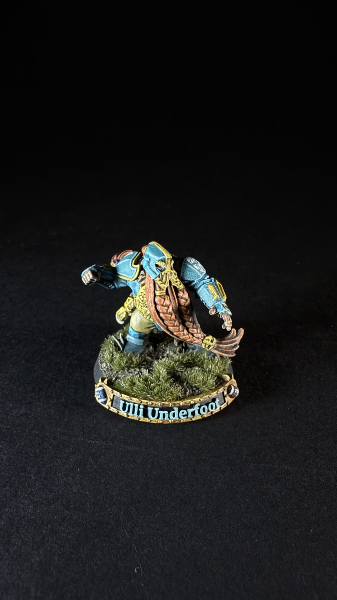 Painted fantasy miniature of a blue-armored warrior with a brown shield, standing on a grassy base; edge text reads 'Ulli Underfoot'.