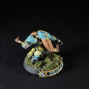 Painted Warhammer 40K Ultramarines miniature in teal-blue armor with gold trim, on a grassy round base with a banner reading Ultramarines.