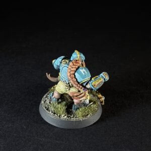 Small painted fantasy miniature of a dwarf in blue armor with yellow trim, shown from the back, standing on a grassy rocky base with a braided brown beard/tail draped over the shoulders.