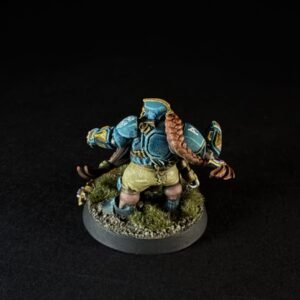 Back view of a blue-armored fantasy miniature with a long braided hair, standing on a rocky, grassy base.