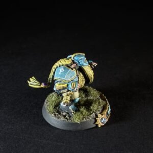 Painted tabletop miniature of a blue-and-yellow armored figure crouching on a grassy base.