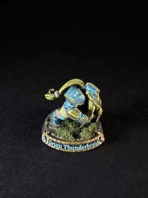 Miniature of Grum Thunderbraid dwarf in blue and gold armor, crouching on a rocky base with tufts of grass.
