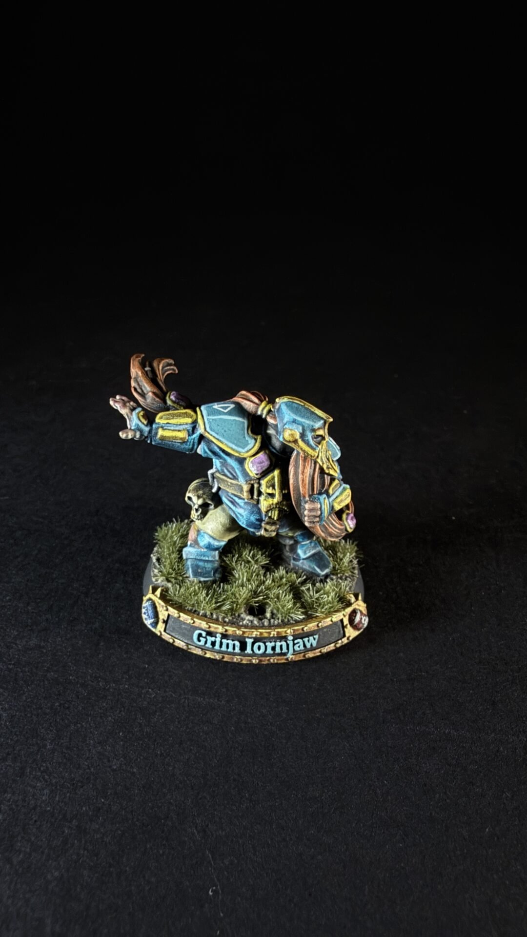Fantasy dwarf miniature in blue armor with yellow trim, standing on a grassy base labeled Grim Ironjaw.