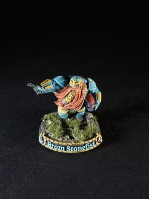 Miniature dwarf warrior in blue armor with an orange beard, standing on a grassy base with a 'Brom Stonefist' banner.