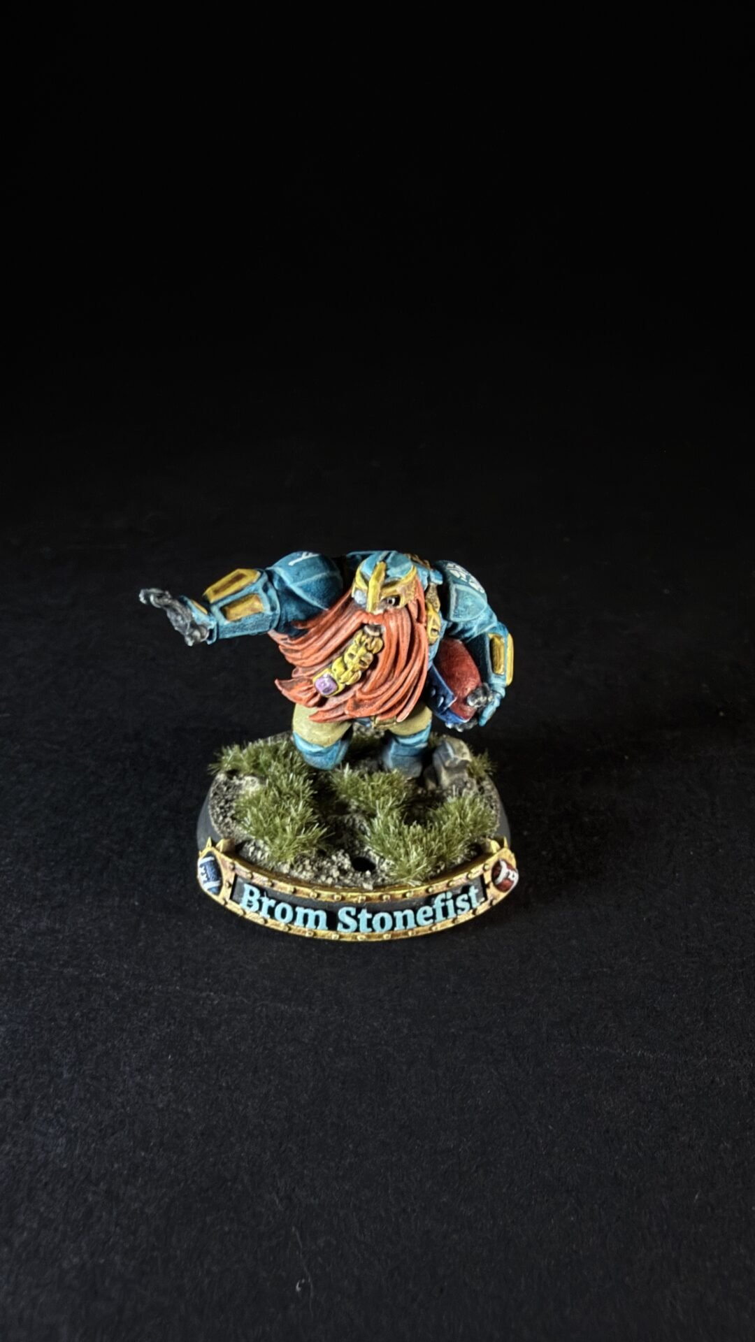 Miniature dwarf warrior in blue armor with an orange beard, standing on a grassy base with a 'Brom Stonefist' banner.