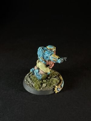 Painted tabletop miniature of a blue-and-gold armored sci‑fi soldier charging forward on a grassy base.