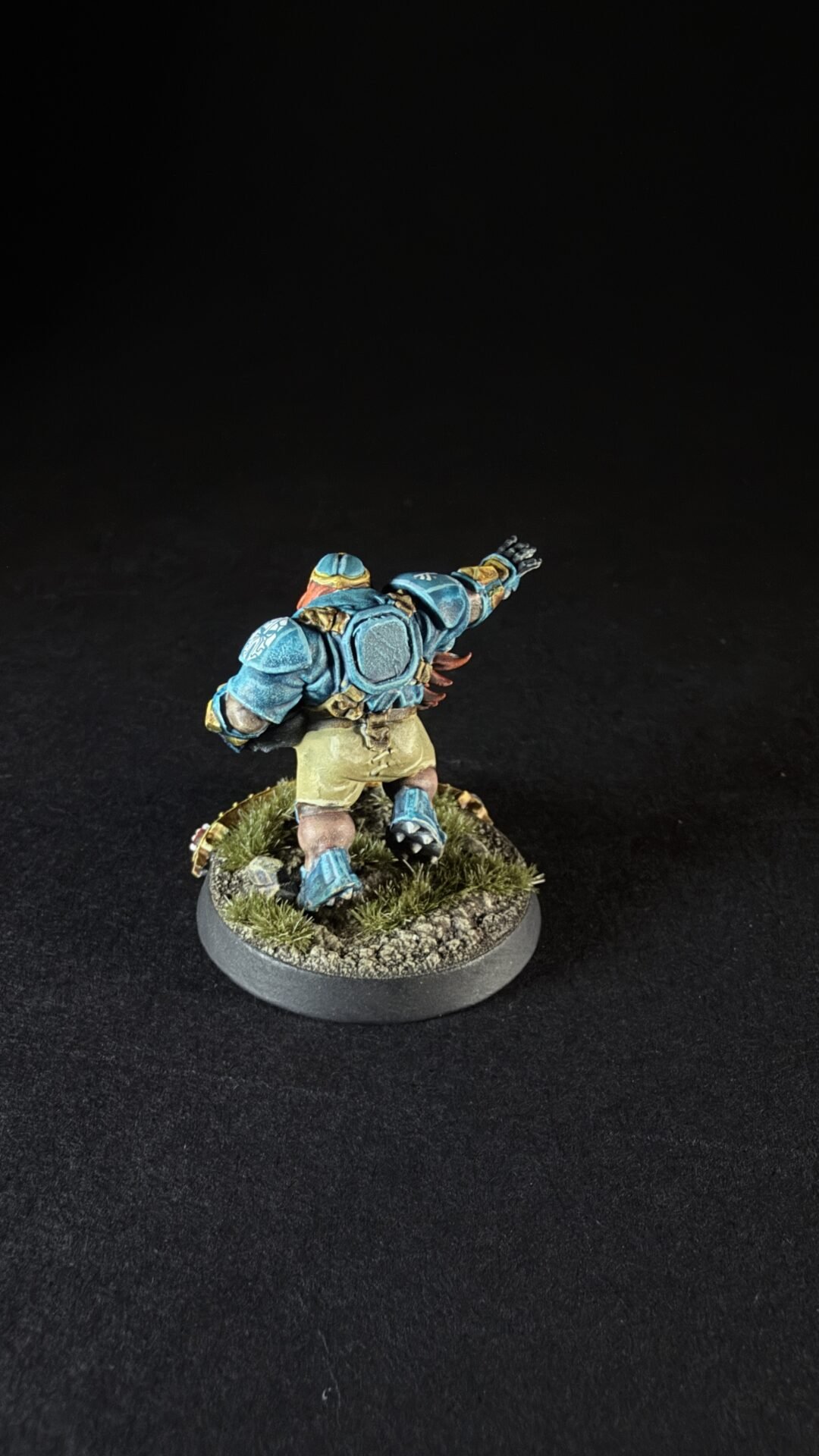 Blue-armored fantasy miniature sprinting on a grassy base, viewed from behind.