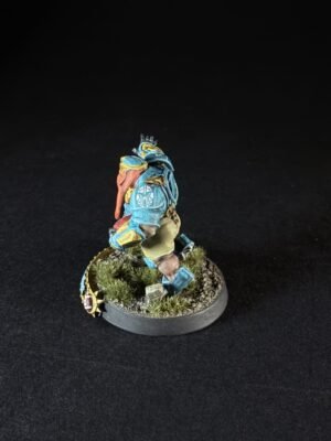 Blue armored miniature figure standing on a grassy round base, posed as if walking forward.