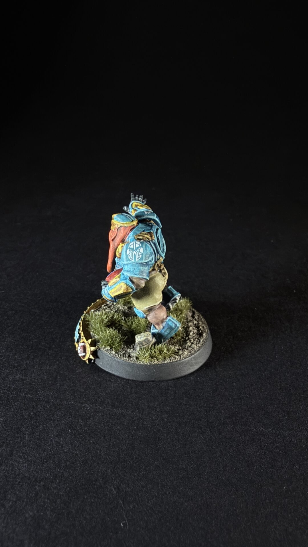 Blue armored miniature figure standing on a grassy round base, posed as if walking forward.