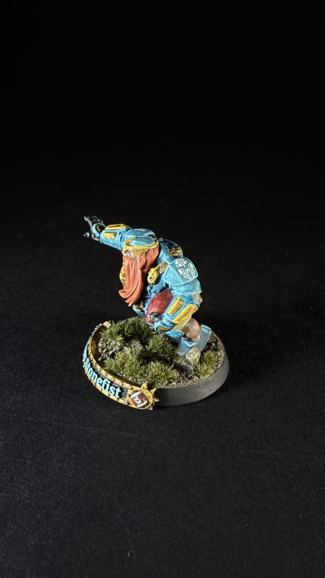 Miniature dwarf warrior in blue armor with an orange beard, raised arm, on a grassy base.