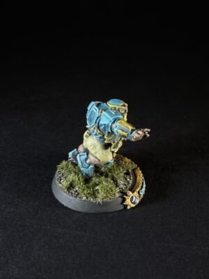 Miniature sci-fi soldier in blue armor sprinting forward, backpack pack and desert-style base with grass tufts on a round base.