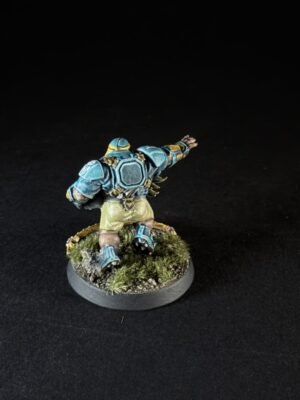 Miniature sci‑fi armored figure seen from behind, blue armor, outstretched right arm, standing on grassy battlefield base.