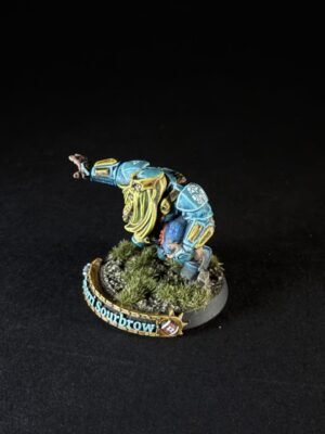 Painted miniature of a dwarf warrior in blue armor with a yellow beard, posed on a grassy diorama base.