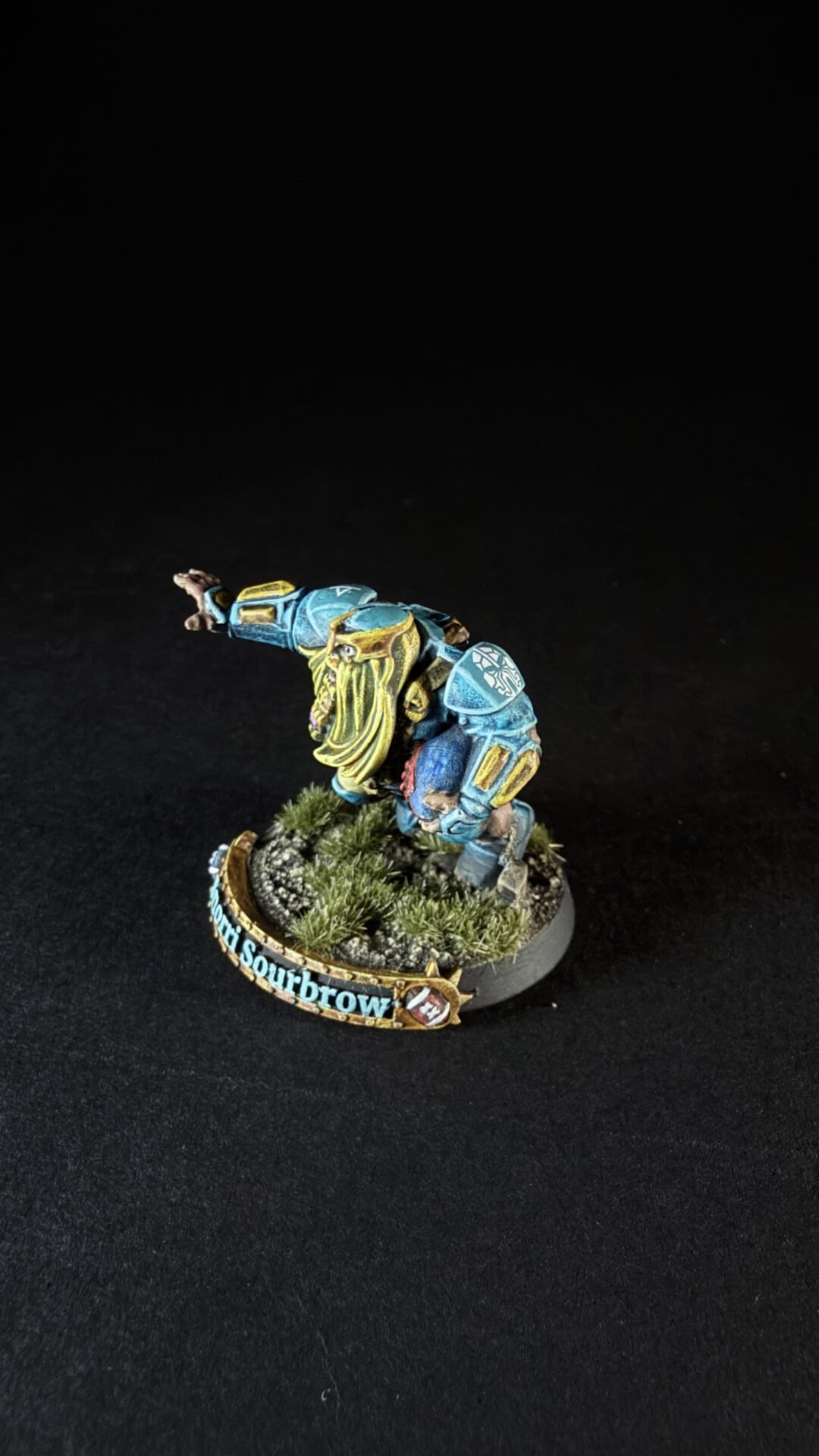 Painted miniature of a dwarf warrior in blue armor with a yellow beard, posed on a grassy diorama base.