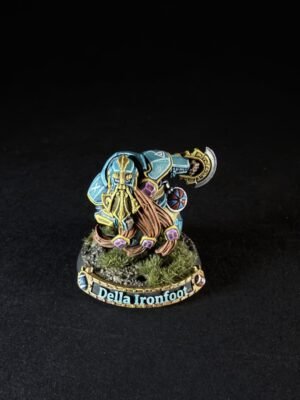 Painted dwarf miniature named Della Ironfoot, wearing blue armor and a golden helm, wielding a large axe on a rocky base with tufts of grass.