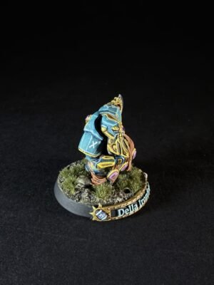 Colorfully painted fantasy miniature: a blue-armored knight with gold trim on a grassy, rocky base, name plaque reading 'Della Iron' (rear view).