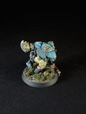 Painted fantasy miniature of a blue-armored warrior with large shoulder plates, standing on a textured grassy base.