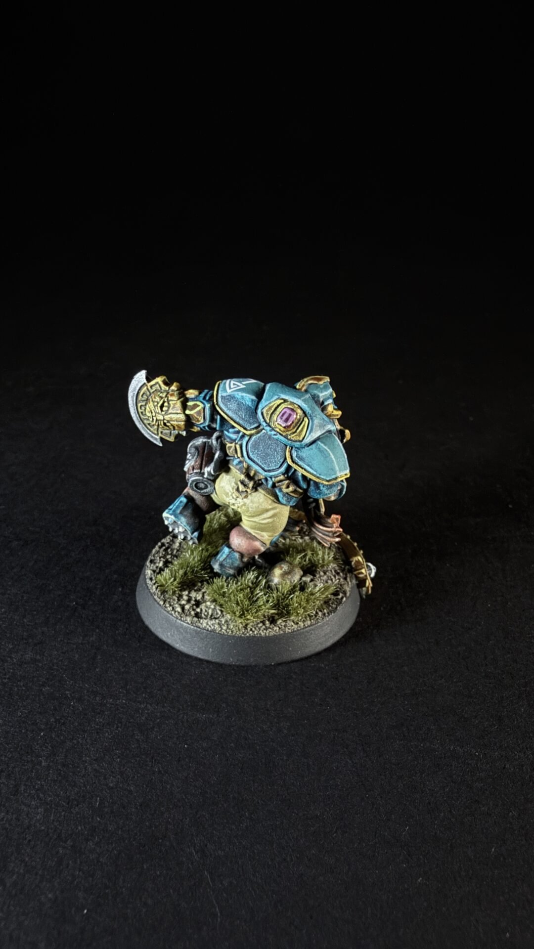 Painted fantasy miniature of a blue-armored warrior with large shoulder plates, standing on a textured grassy base.