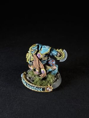 Painted dwarf miniature named Della Ironfoot, in teal armor, wielding an axe and shield, on a grassy base with tufts of grass.