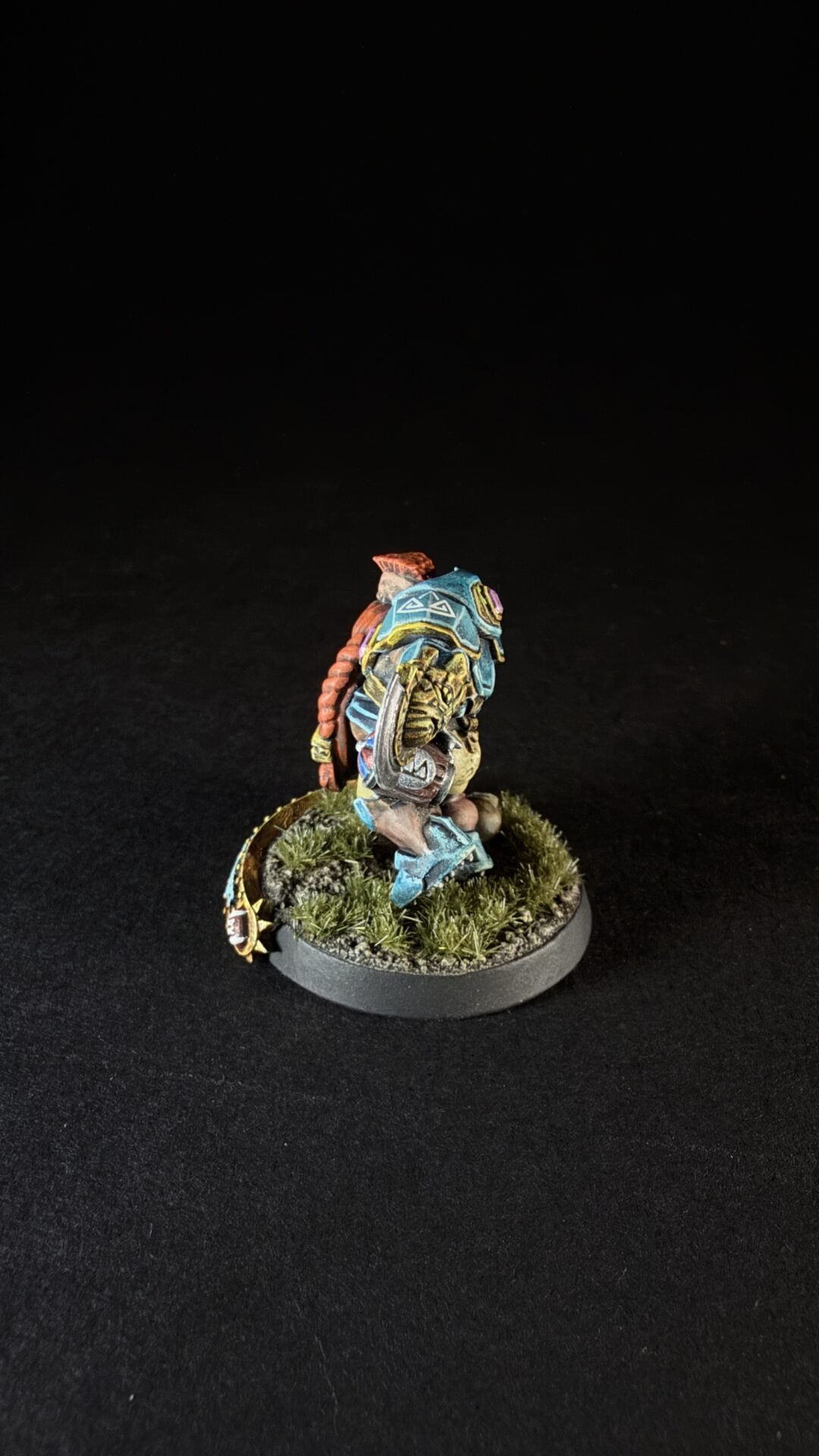 Painted fantasy miniature: a heavily armored figure in teal-blue armor on a grassy round base, posed as if advancing.