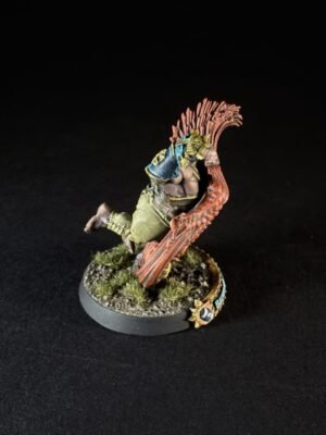 Painted fantasy miniature of a green orc-like warrior leaping with a large red spiked crest or wing behind him, on a rocky base with tufts of grass.