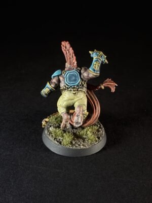 Back view of a painted fantasy miniature wearing blue armor and yellow shorts, with a red tail and a grassy rocky base.