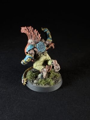 Back view of a painted fantasy miniature: a muscular winged humanoid in teal armor, khaki shorts, leaping on a rocky, grassy base.