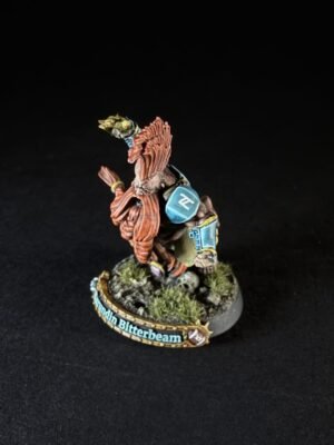 Painted tabletop miniature of a winged creature with red feathers and blue armor, standing on a grassy base with a name banner reading 'Gundin Bitterbeam'.