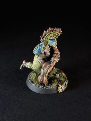 Tabletop miniature of a muscular orc/barbarian-wearing blue armor, mid-stride on a grassy base, with a decorative shield on its back.