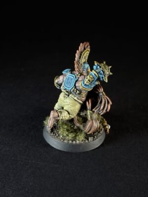 Miniature figure, a armored fantasy warrior with blue armor and large winged back, posed on a grassy base against a black background, viewed from behind.