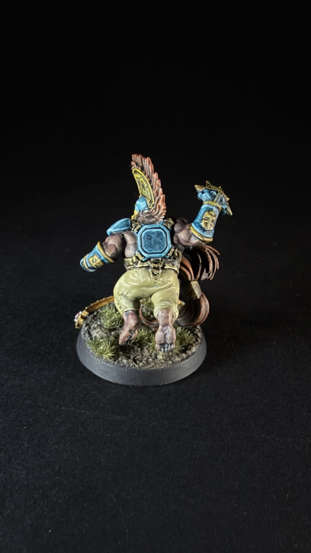 Back view of a fantasy miniature rider in blue armor on a beast, standing on a grassy base.