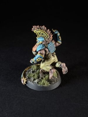 Miniature orc warrior in blue armor with a feathered headdress, posed mid-step on a grassy base against a black backdrop.