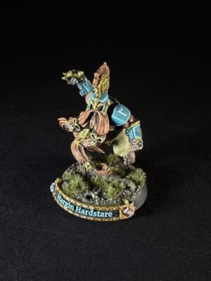Painted fantasy miniature: a muscular warrior with blue armor perched on a mossy base, mid-action pose, banner on the base reads 'Hargin Hardstare'.